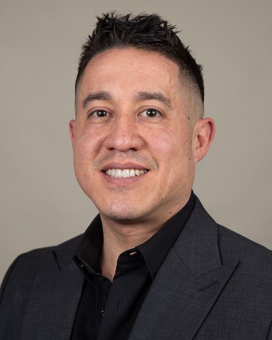 Studio headshot, black shirt, warm gray backdrop